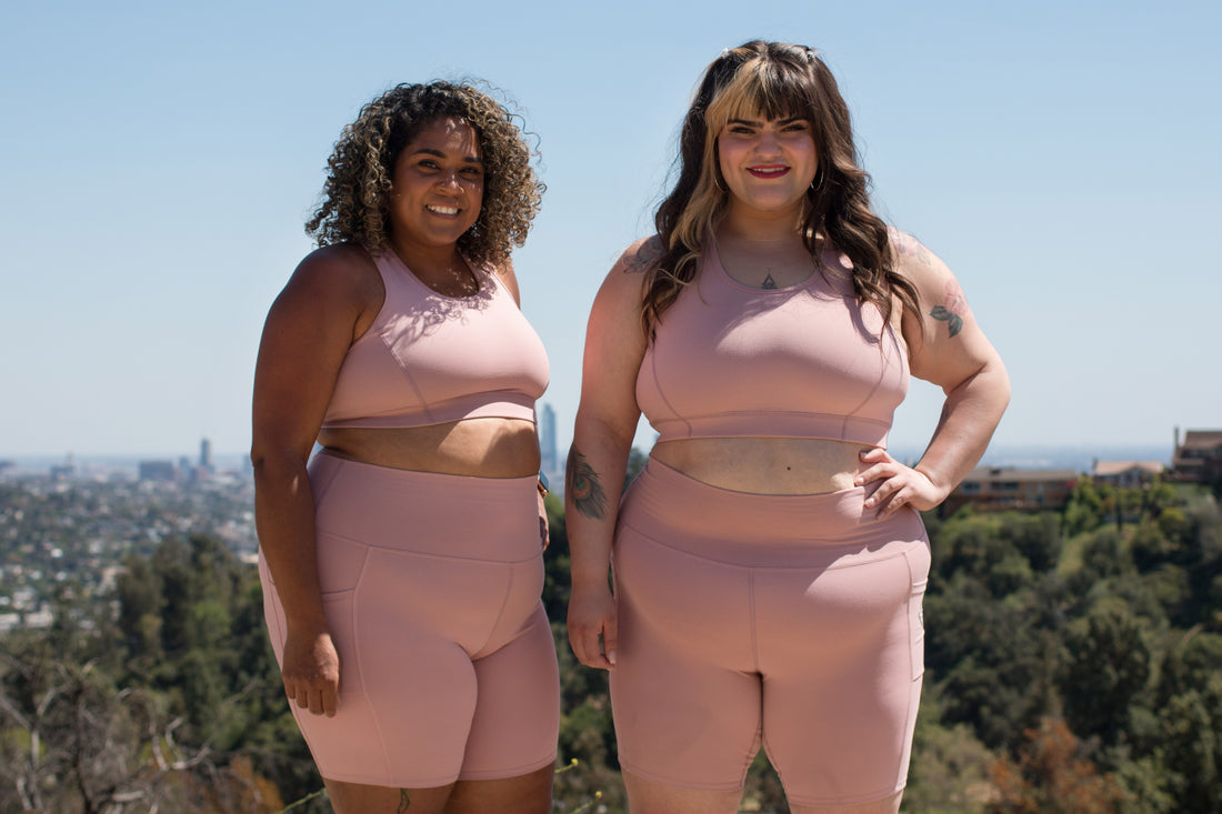 Two plus size women are hiking outdoors in Superfit Hero bike shorts and sports bras. 
